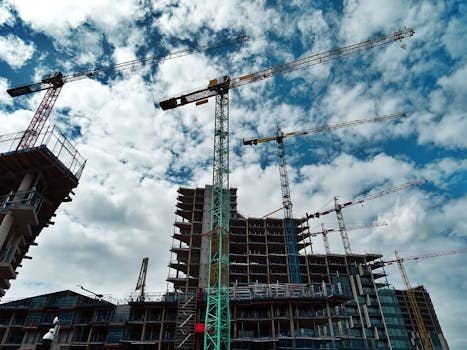 Urban construction site with numerous cranes framing rising skyscrapers against a blue sky.